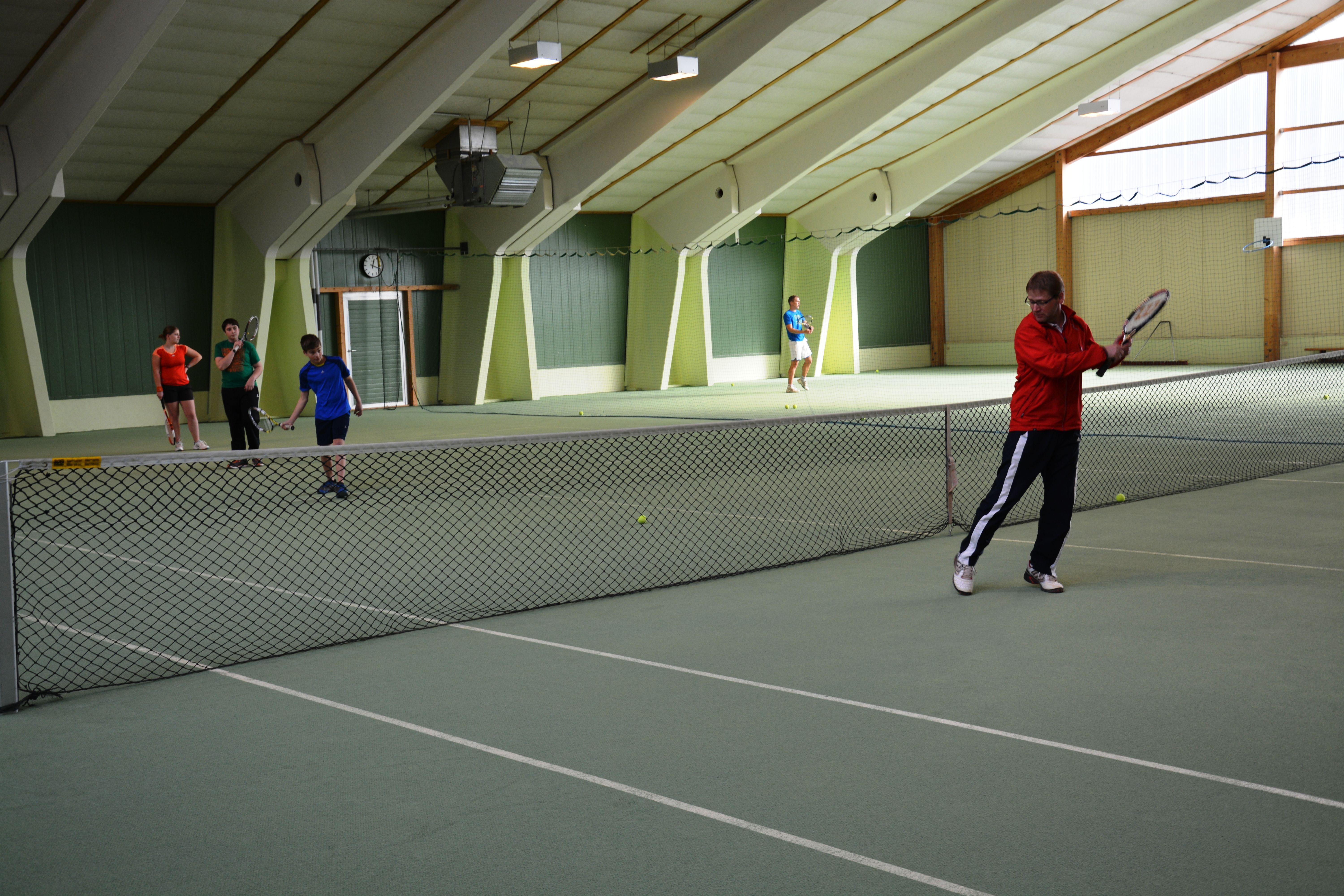 Lidé hrají tenis v krytém tenisovém centru.