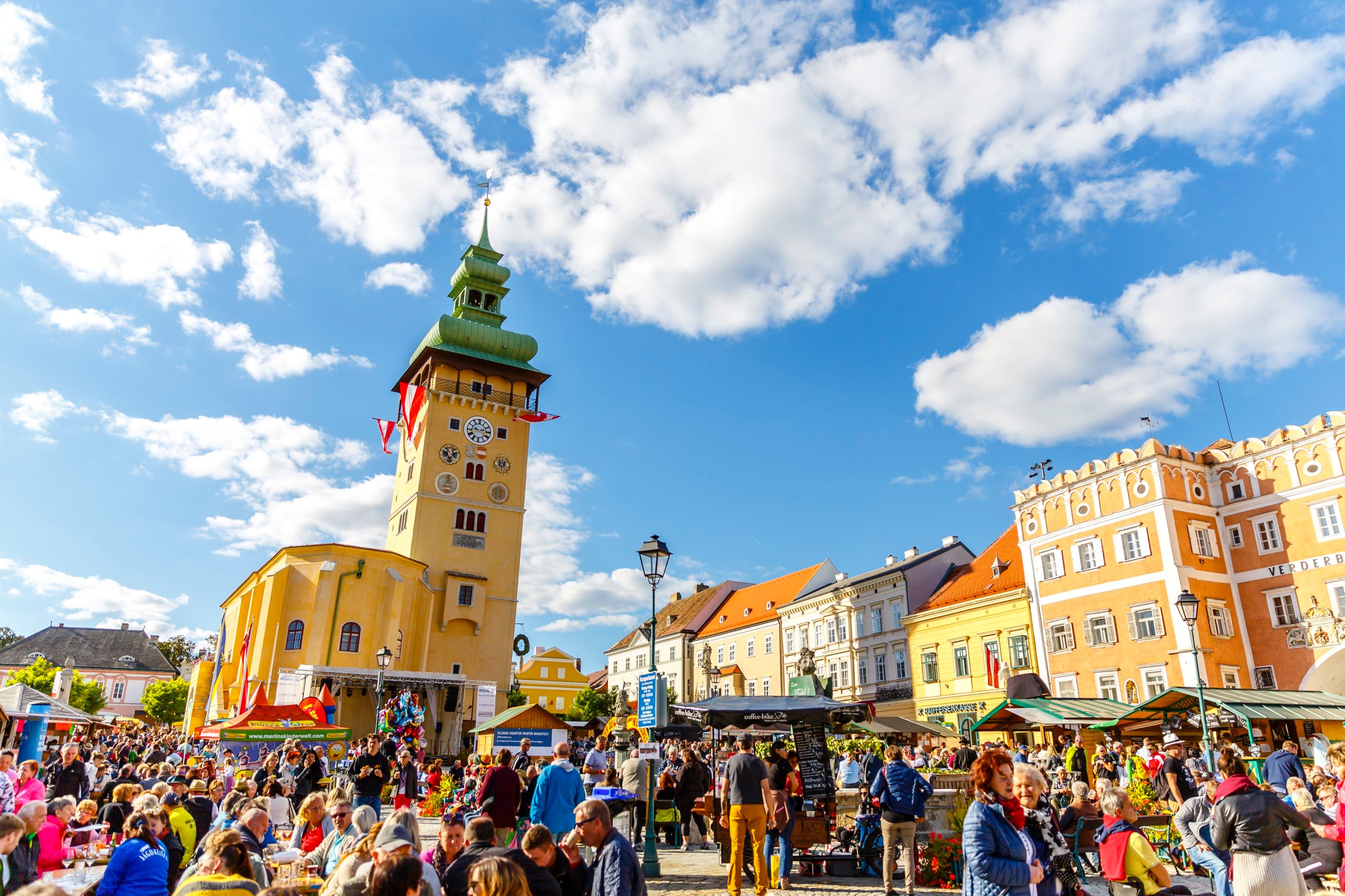 Dav lidí na rušném náměstí v Retzu s výraznou hodinovou věží v pozadí.