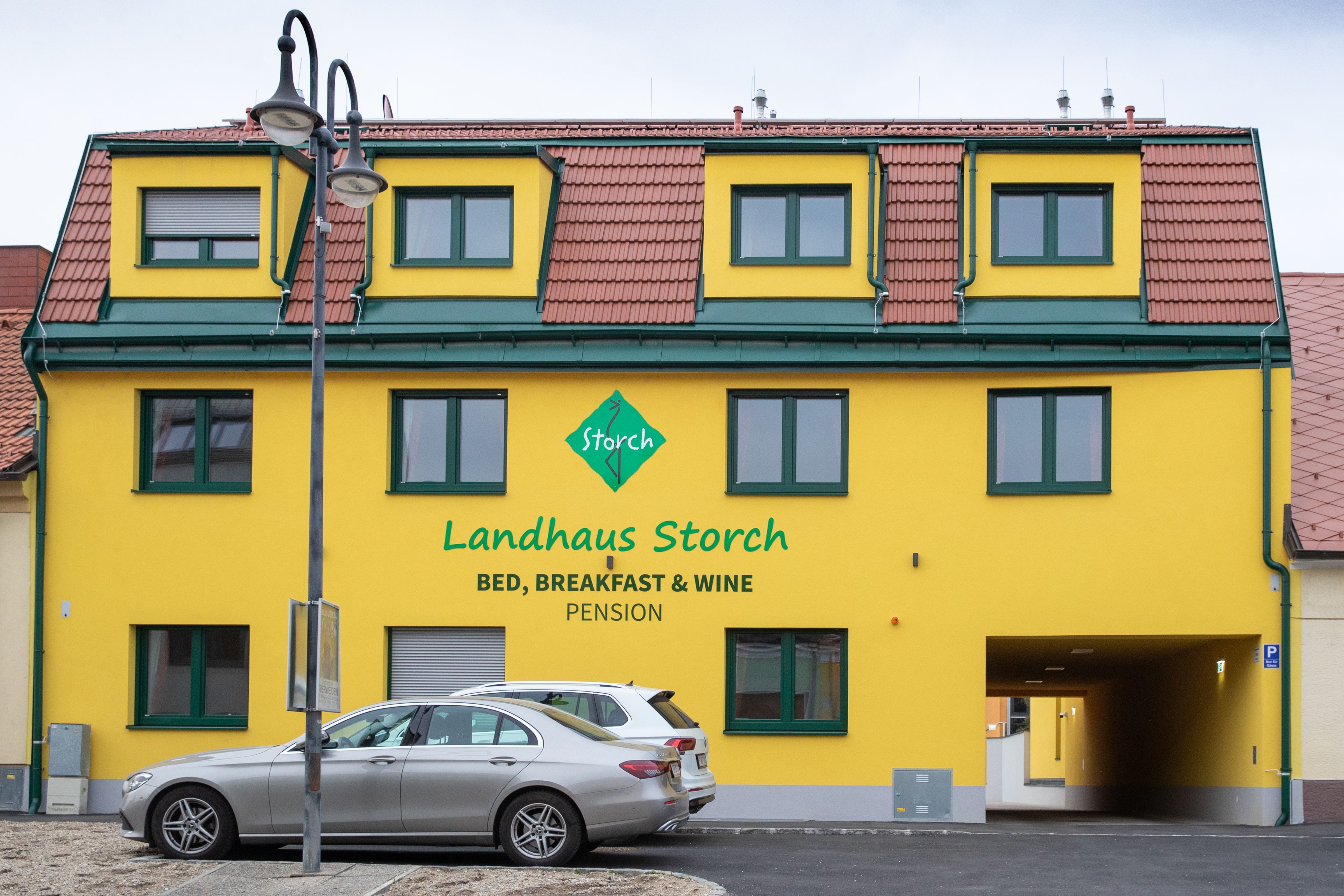 Žlutá budova s nápisem "Landhaus Storch", před ní zaparkovaná auta.