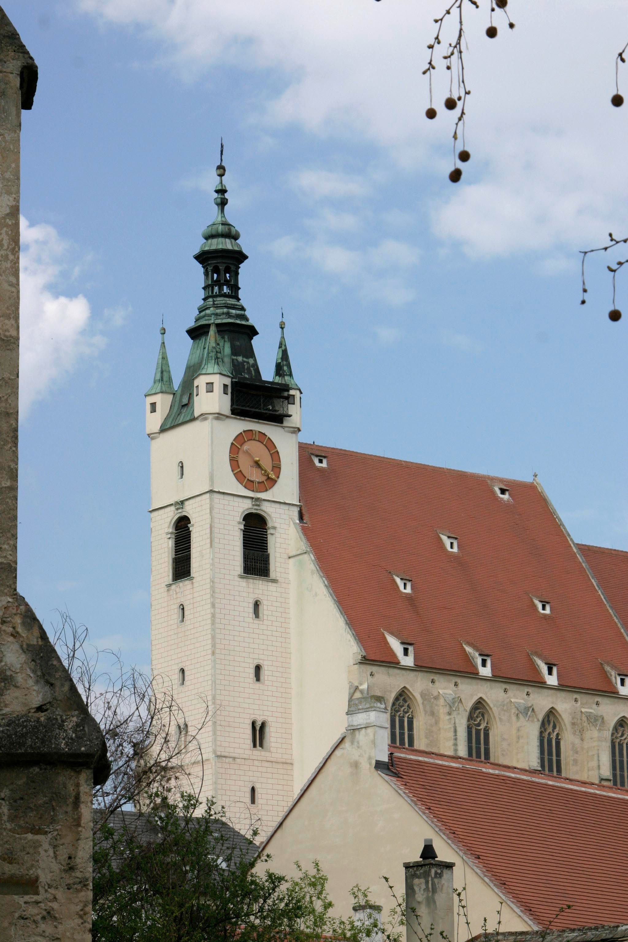 Piaristický kostel s věží a hodinami na pozadí modré oblohy.