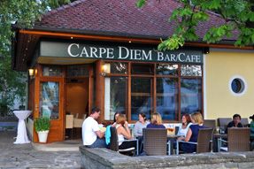 Pohled zvenčí na kavárnu Carpe Diem, lidé sedí u venkovních stolků.