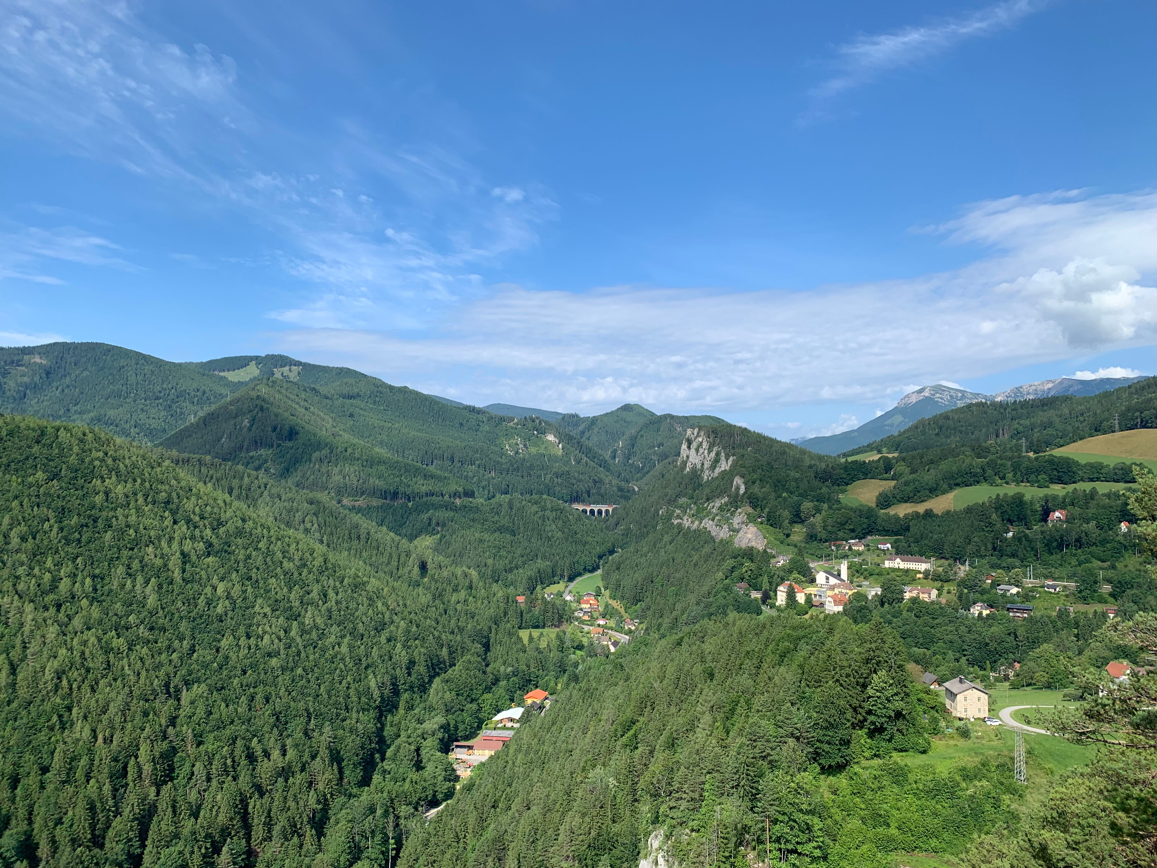 Panoramatický pohled na zelenou horskou krajinu s malou vesnicí a viaduktem.