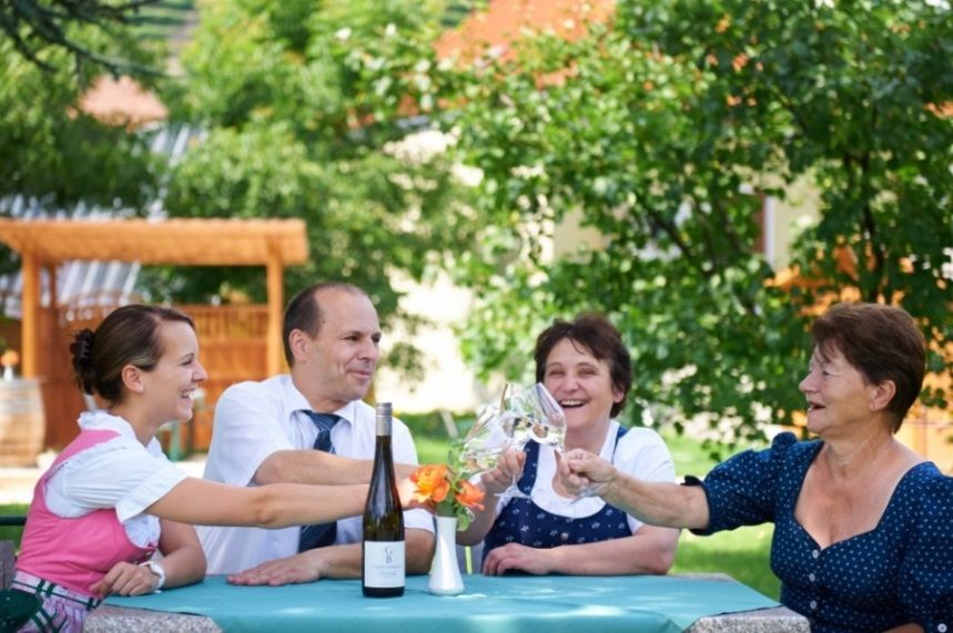 Čtyři lidé si u venkovního stolu cinknou skleničkami vína.