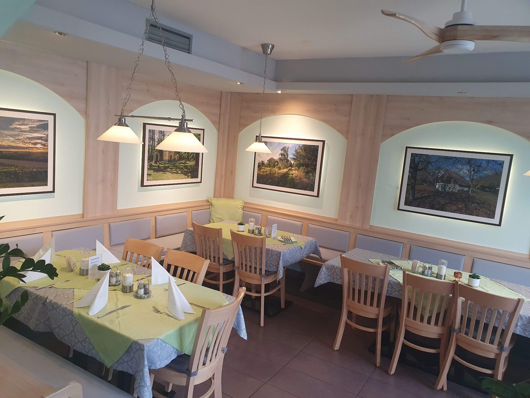 Pohled do interiéru restaurace s dřevěným nábytkem a dekorativními obrazy na stěnách.