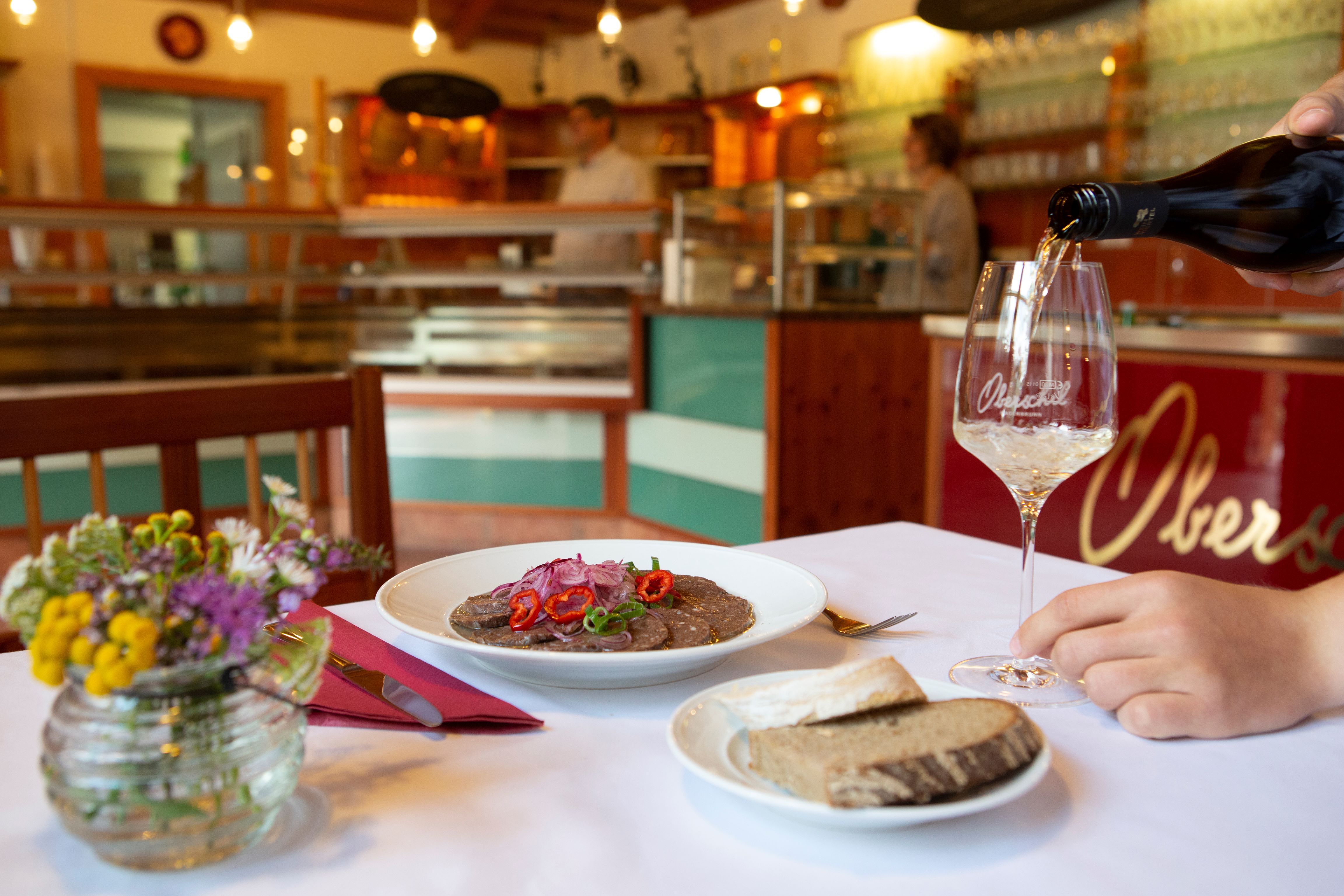 Prostřený stůl ve vinárně s talířem jídla, chlebem a sklenkou vína.