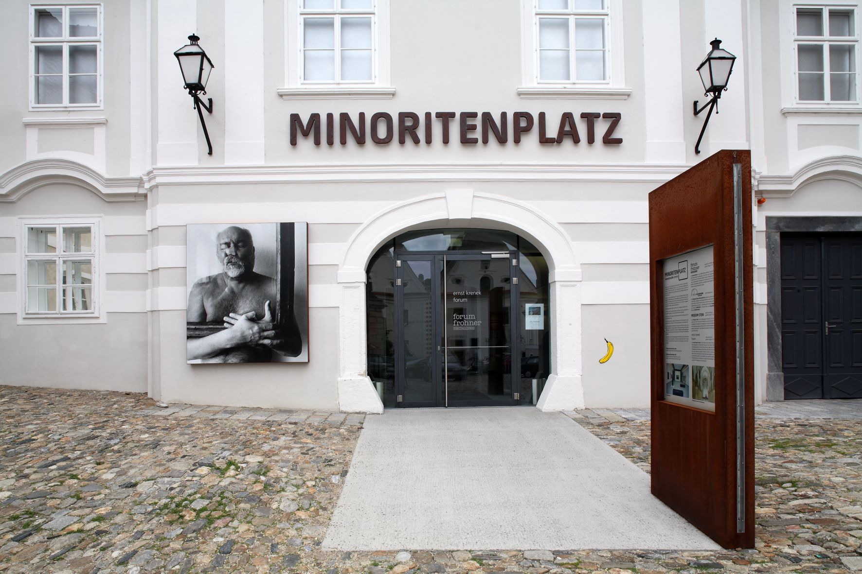 Vstup do Fóra Frohner na náměstí Minoritenplatz s uměleckou fotografií a informační tabulí.