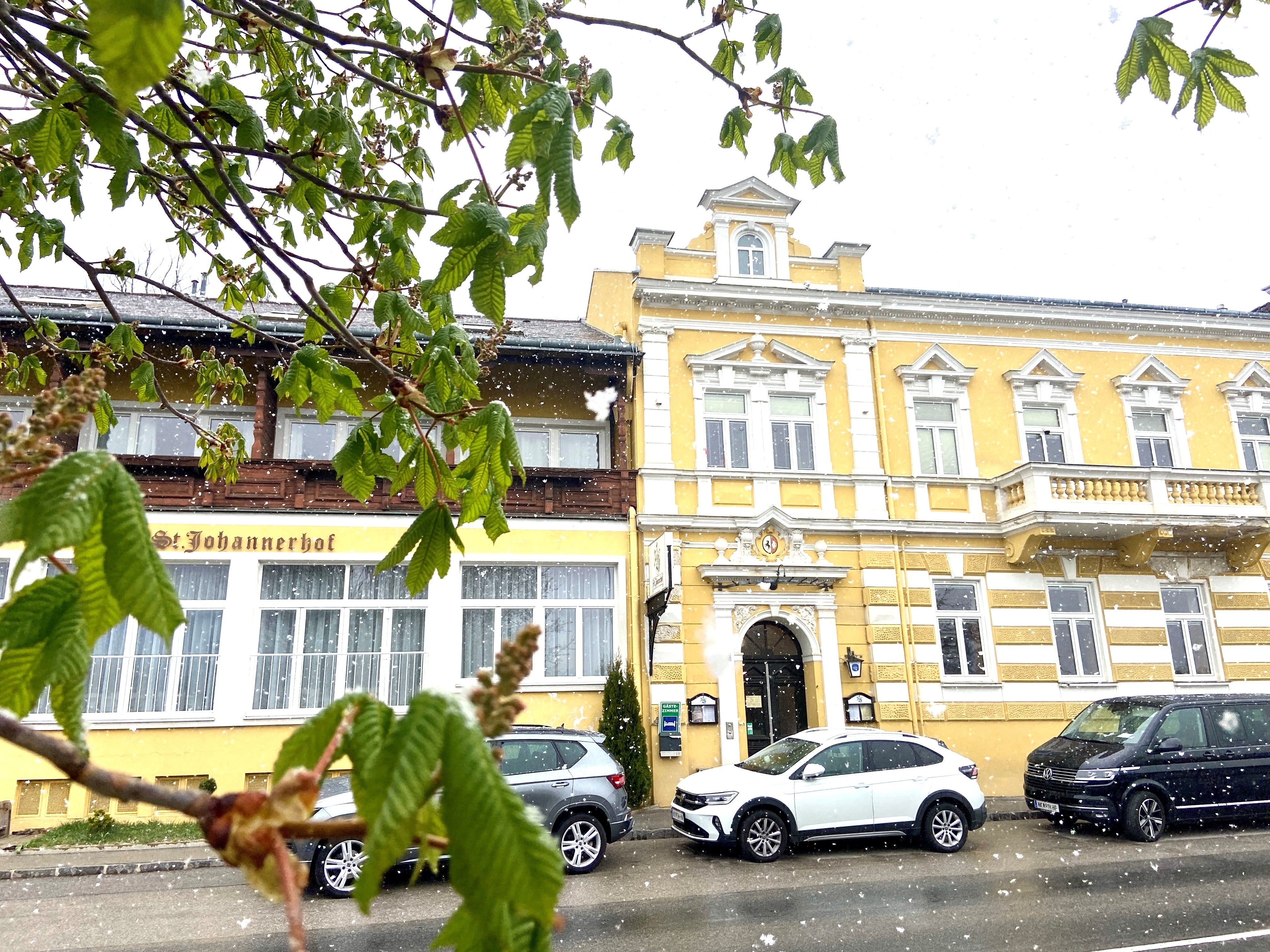 Žlutá budova zámku Sankt Johannerhof se zasněženými auty před ní a zeleným listím v popředí.