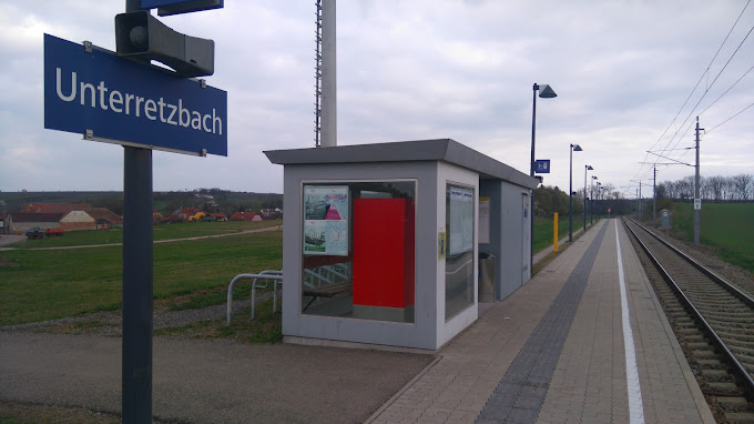 Malé nádraží Unterretzbach s autobusovým přístřeškem a železničními kolejemi.