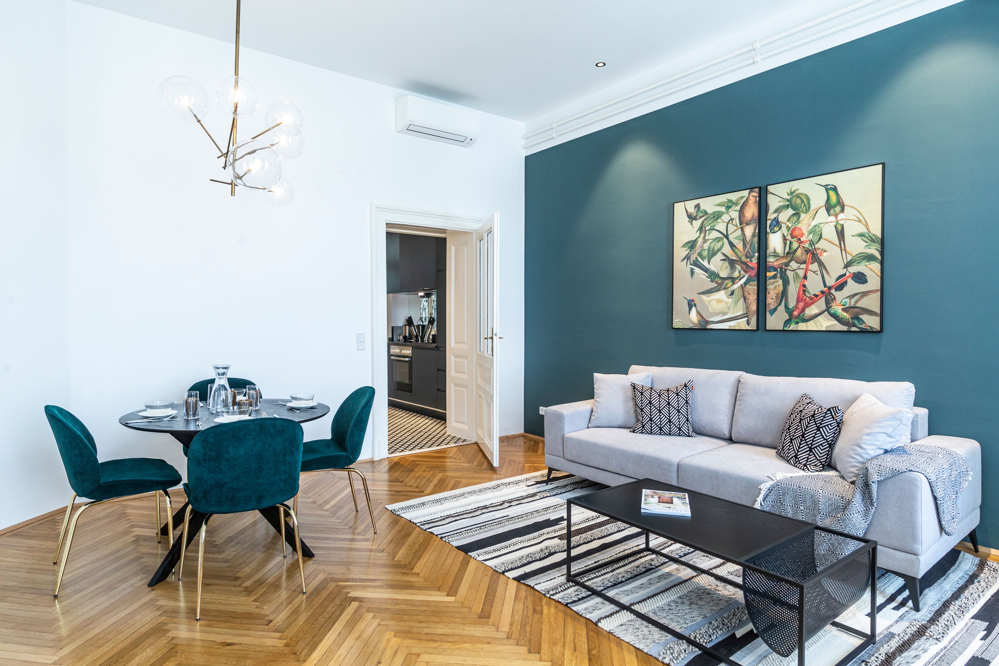 Moderní obývací pokoj s šedou pohovkou, jídelním stolem a uměleckými díly na stěně.