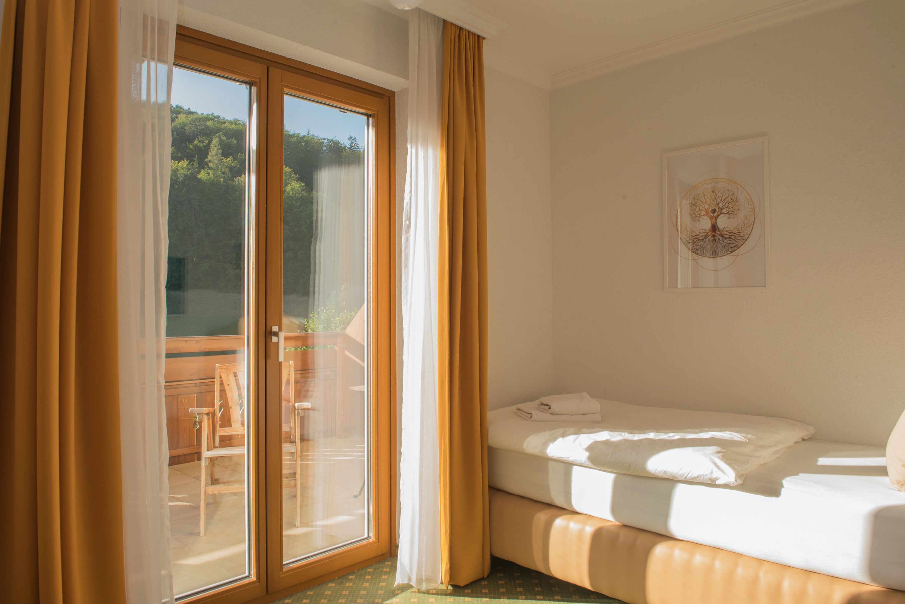 Jednolůžkový pokoj s balkonem, postel, žluté závěsy, dřevěný balkon, slunný.