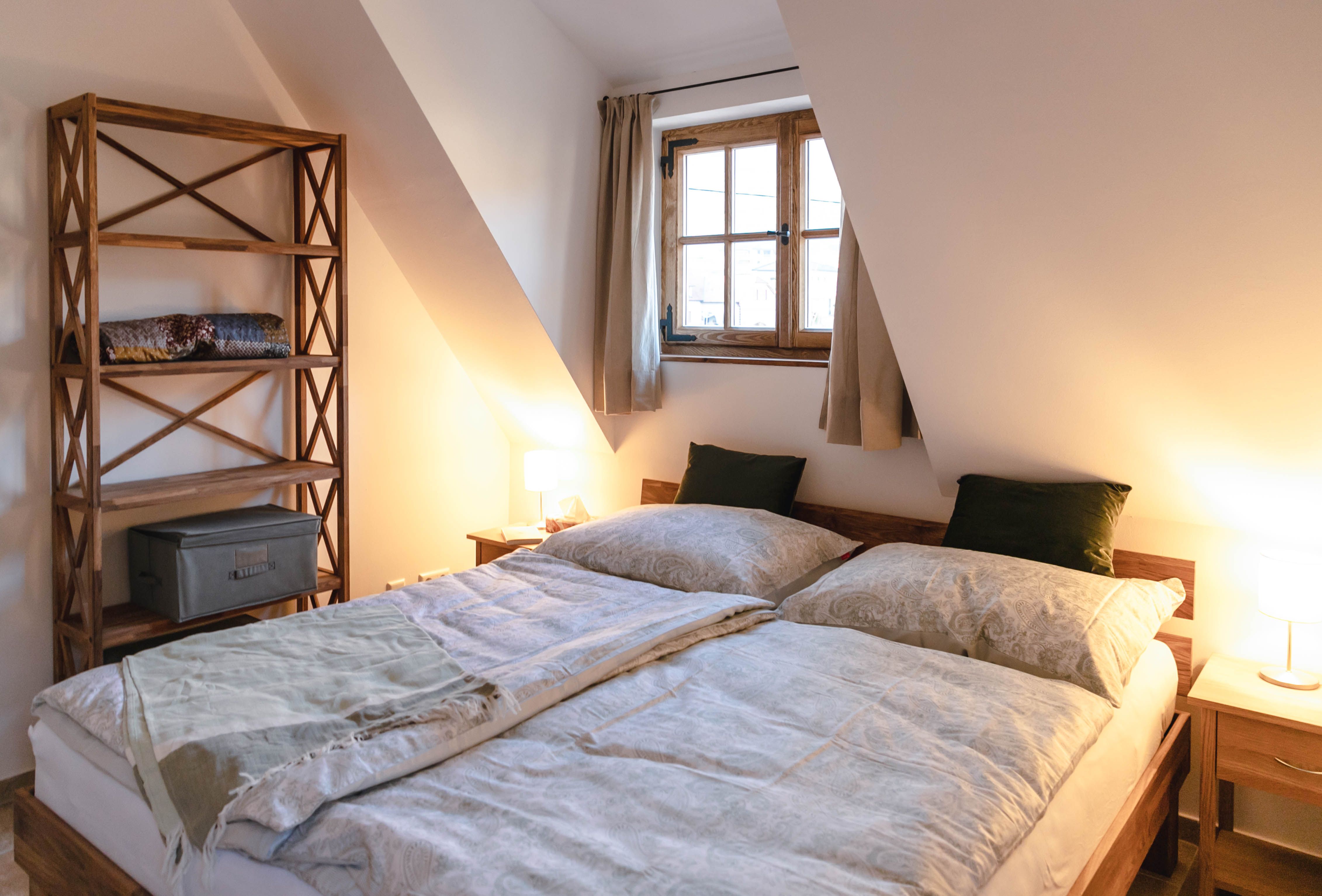 Útulná ložnice s manželskou postelí, dřevěnou knihovnou a oknem se závěsy.