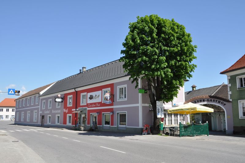 Gasthof Wegl na cestě se stromem a slunečníky.