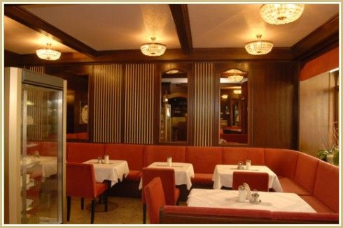 Pohled do interiéru elegantní restaurace s červenými lavicemi a bílými ubrusy.