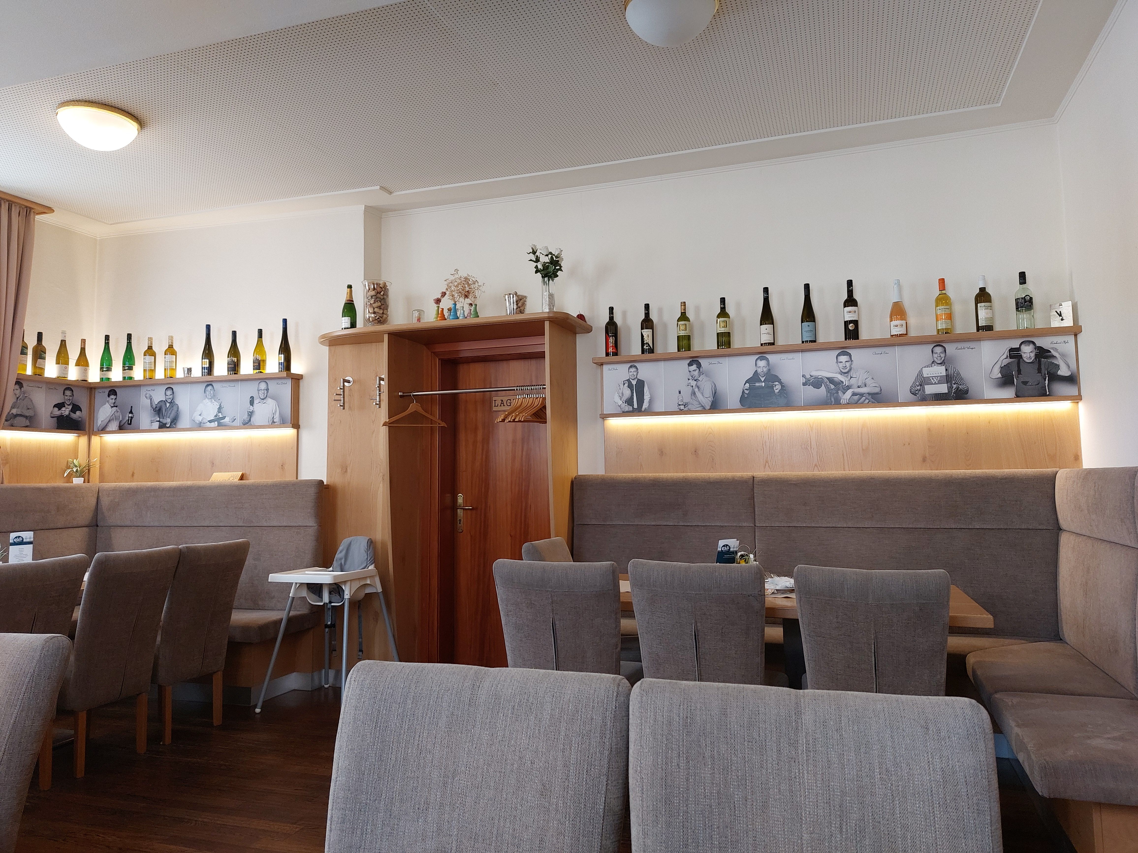 Pohled do interiéru restaurace s lahvemi vína a černobílými fotografiemi na stěně.