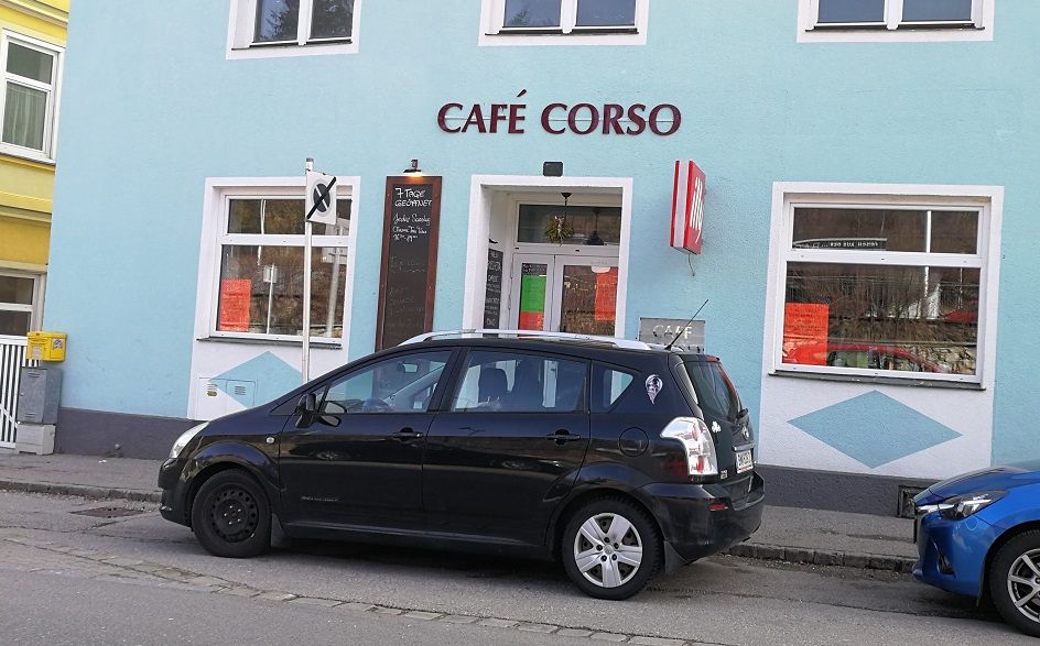 Pohled zvenčí na kavárnu Café Corso a zaparkované auto před ní.