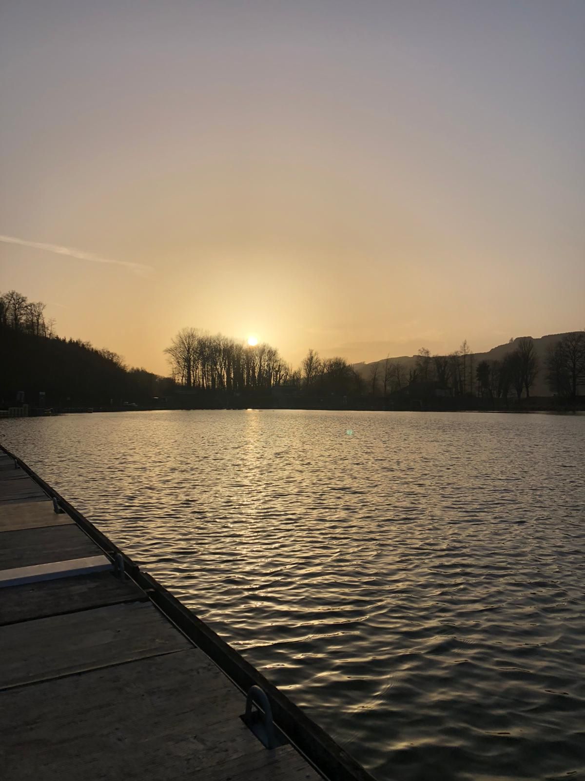 Západ slunce nad přístavem s molem a stromy v pozadí.