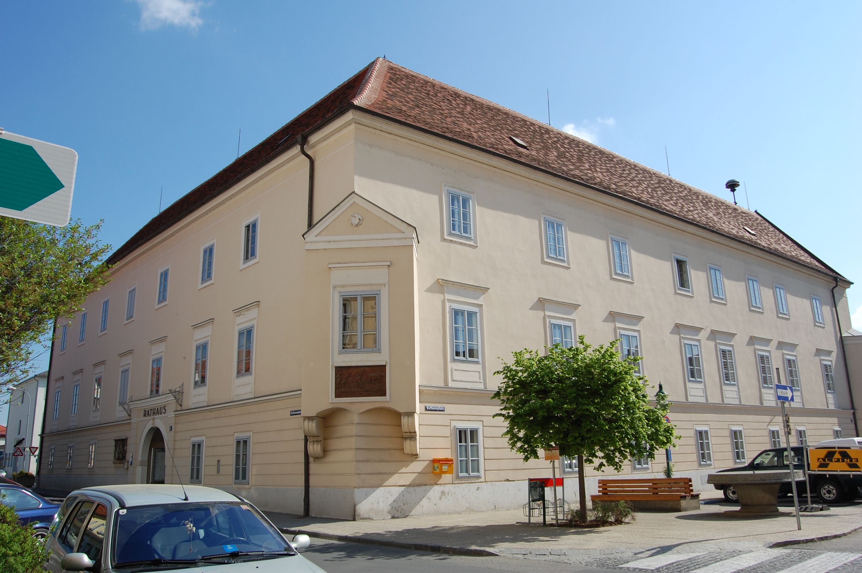 Velká světlá budova s červenými střešními taškami a mnoha okny, označená jako "radnice".