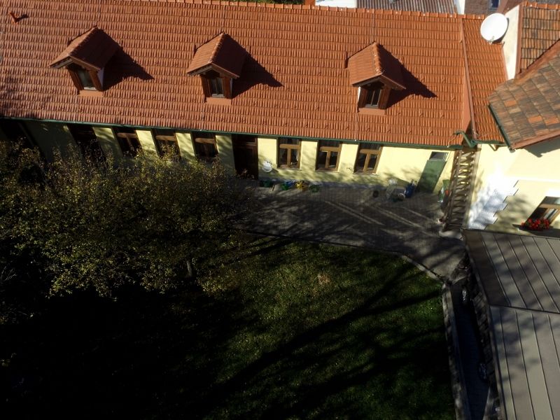 Letecký pohled na budovu s červenou taškovou střechou a několika okny, obklopenou zahradou.