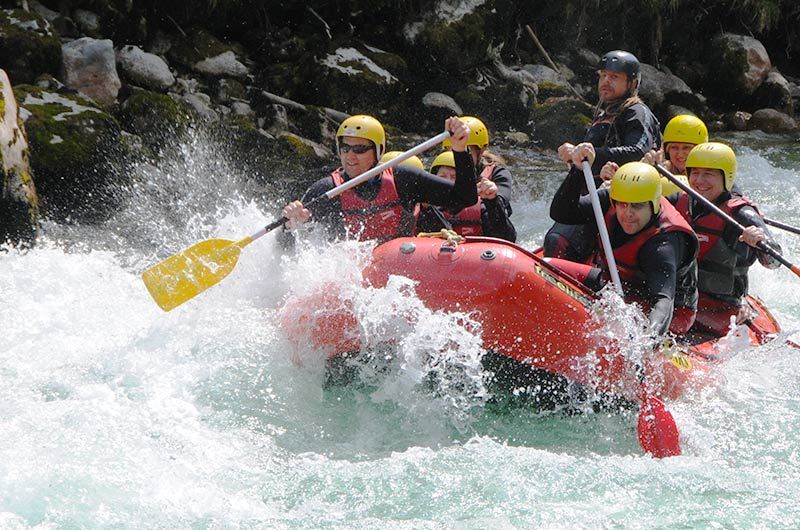 Skupina na raftu na řece se žlutými helmami a červenými vestami.