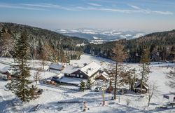Lyžařský areál se sedačkovou lanovkou a lyžaři, obklopený zasněženými stromy a kopci.