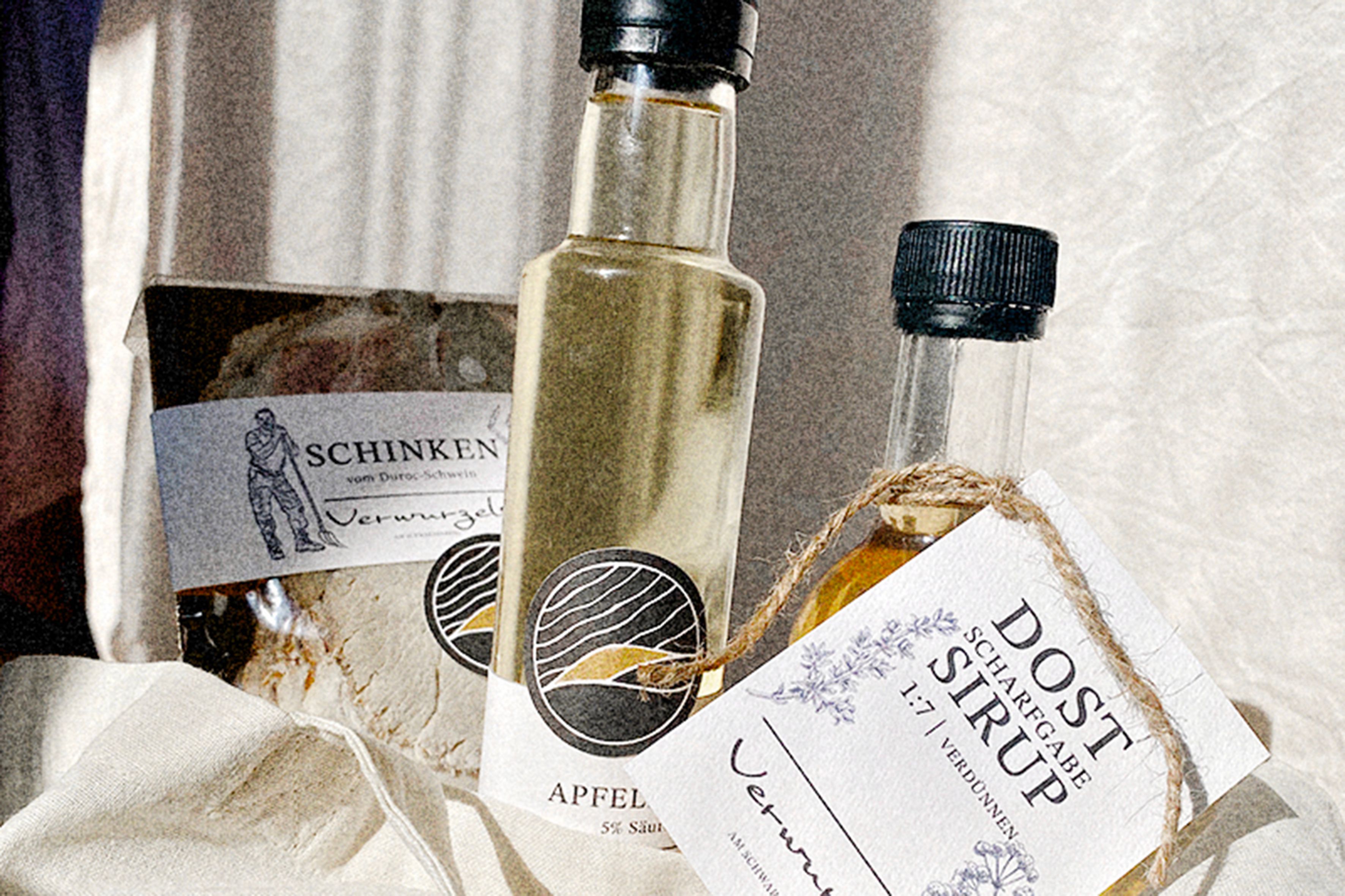 Detailní záběr na šunku, jablečný ocet a sirup s etiketami na utěrce.