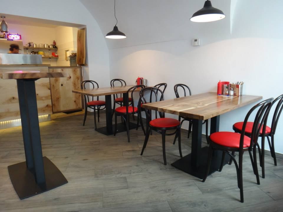 Pohled do interiéru moderní restaurace s dřevěnými stoly a červenými židlemi.