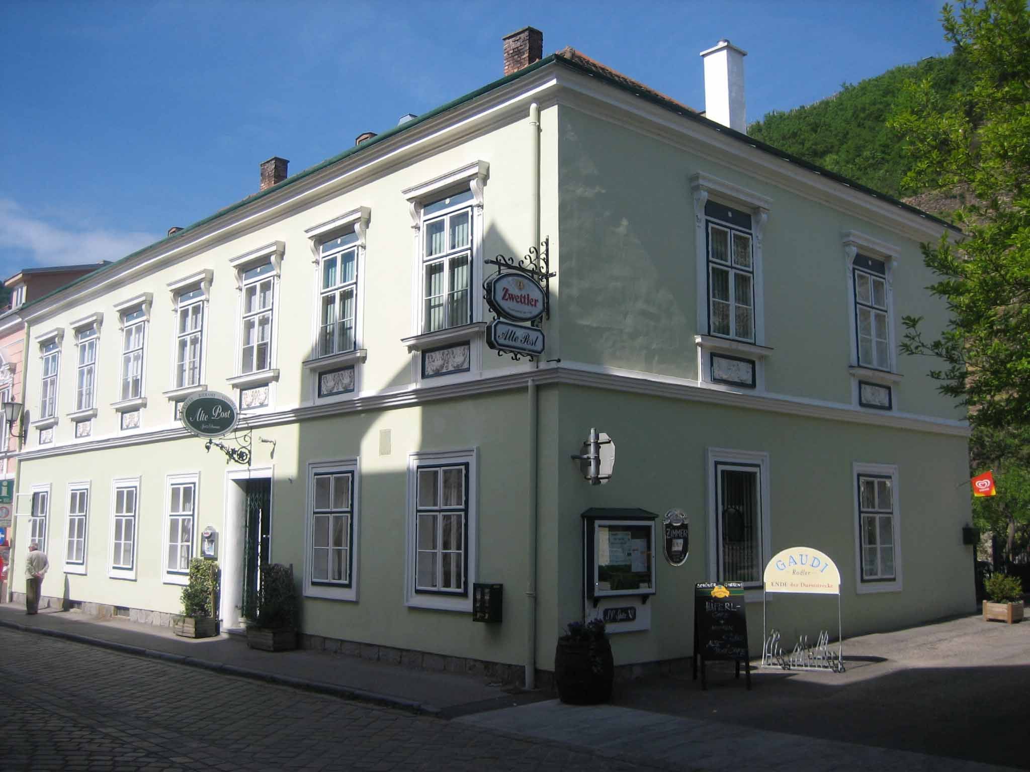 Historická budova se zelenou fasádou a několika okny, označená jako hostinec.