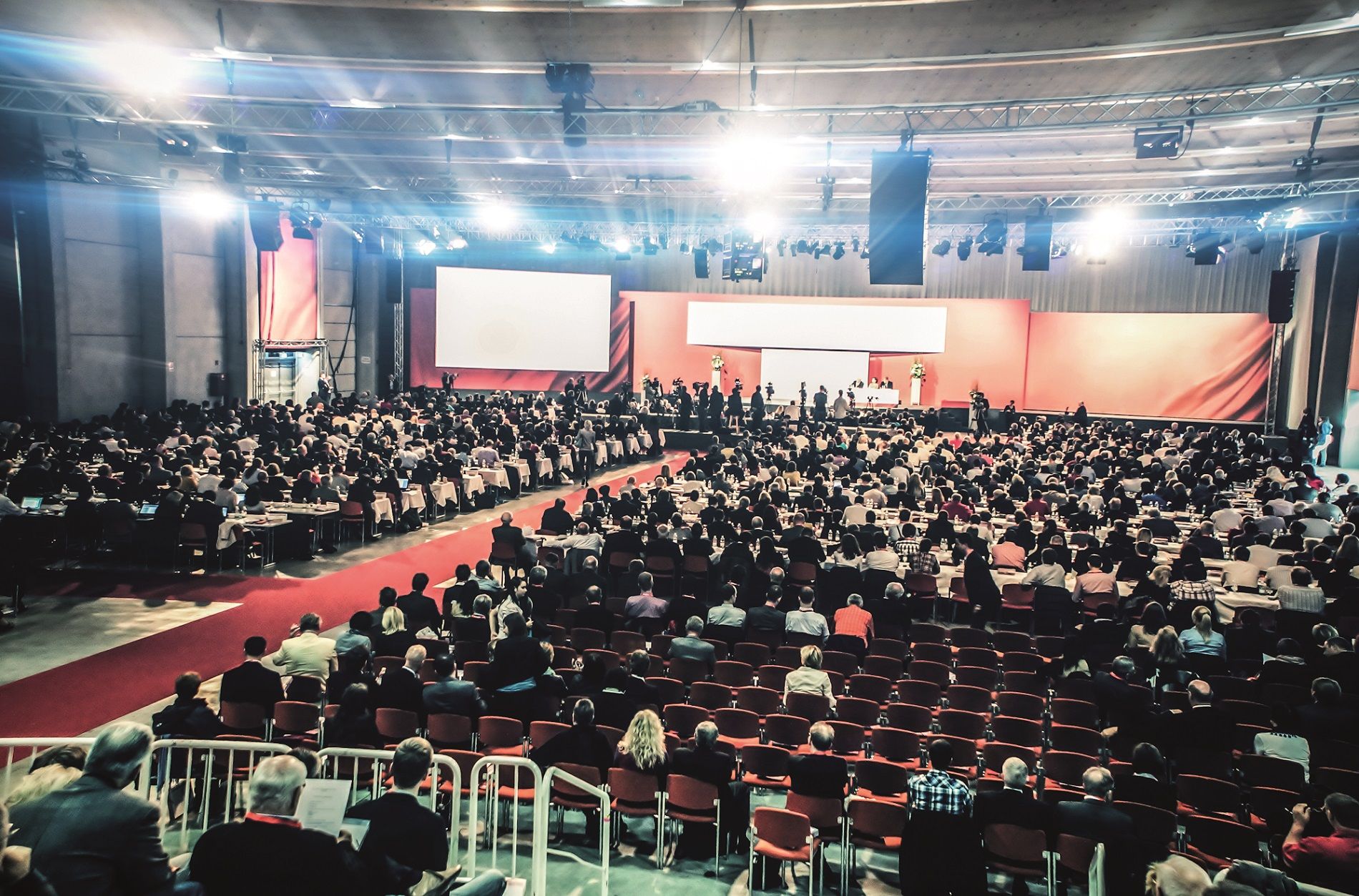 Velký kongresový sál s mnoha účastníky, jevištěm a plátnem.