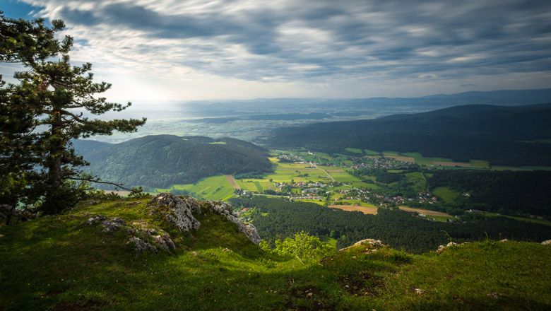 Pohled z okraje útesu na zelenou krajinu s kopci a vesnicí v údolí.