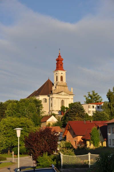 Poutní kostel na kopci s červenými střechami a stromy v popředí.