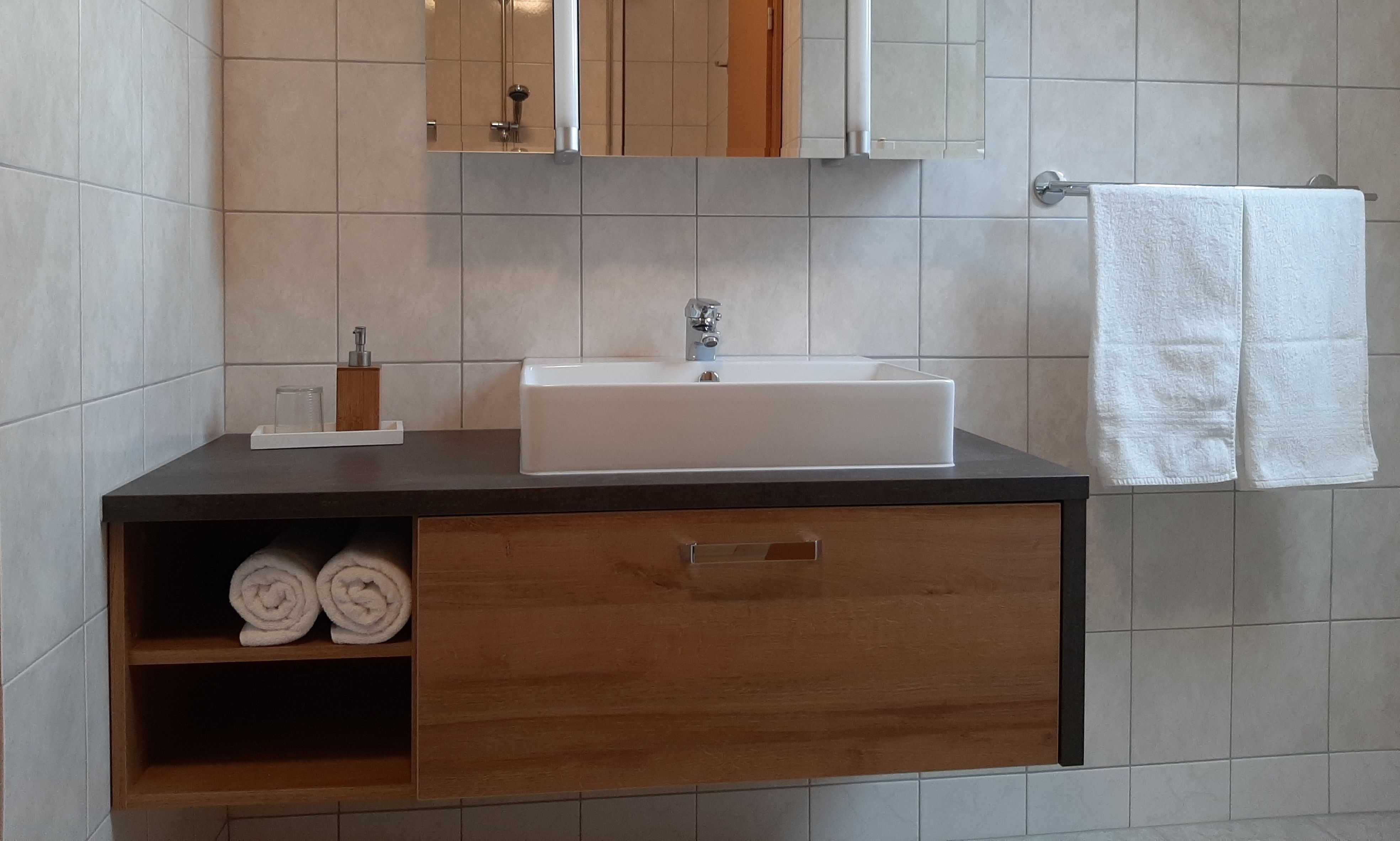 Moderní koupelna s umyvadlem, ručníky a zrcadlem.
