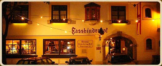 Noční záběr na budovu s nápisem "Fassbinderhof", osvětlenou pohádkovými světly.