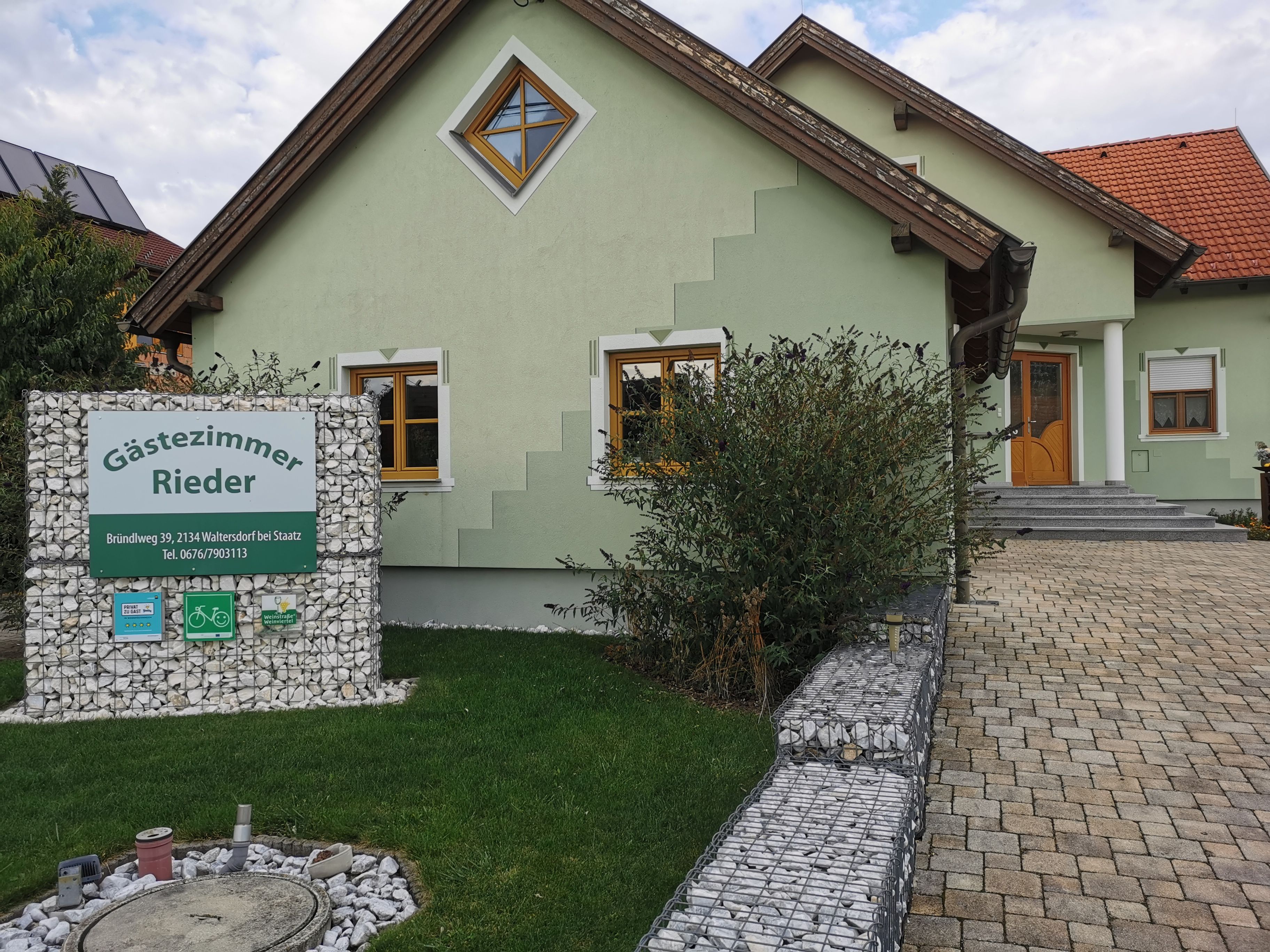 Zelený domek s nápisem "Gästezimmer Rieder" v předzahrádce.