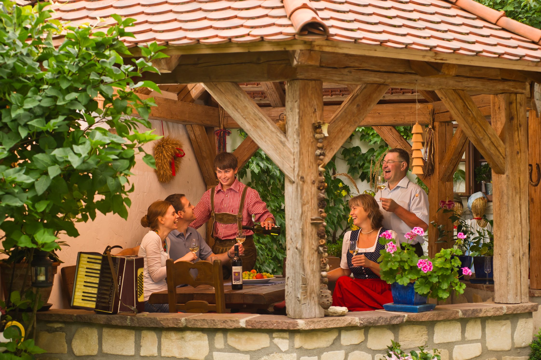 Skupina lidí sedí v zastřešeném rustikálním pavilonu a vychutnává si víno a společnost.