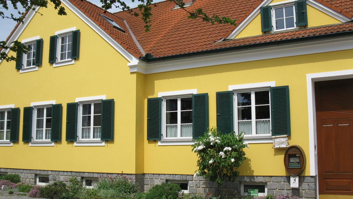 Žlutý dům se zelenými okenicemi a červenou taškovou střechou.