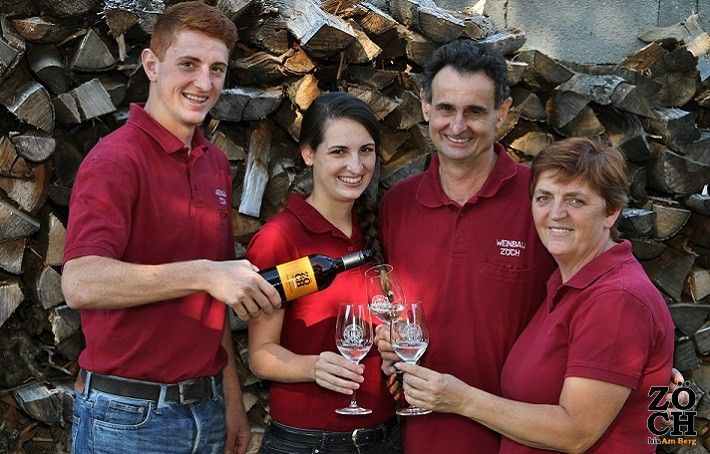 Čtyři lidé v červených košilích cinknou skleničkami vína před hromadou klád.