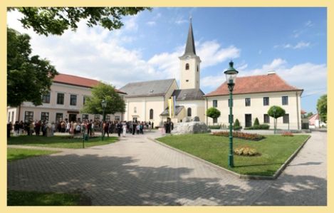 Absdorfský farní kostel s okolním náměstím a shromážděním lidí.