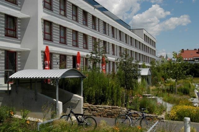 Moderní několikapatrová budova obklopená zelenou krajinou s jízdními koly v popředí.