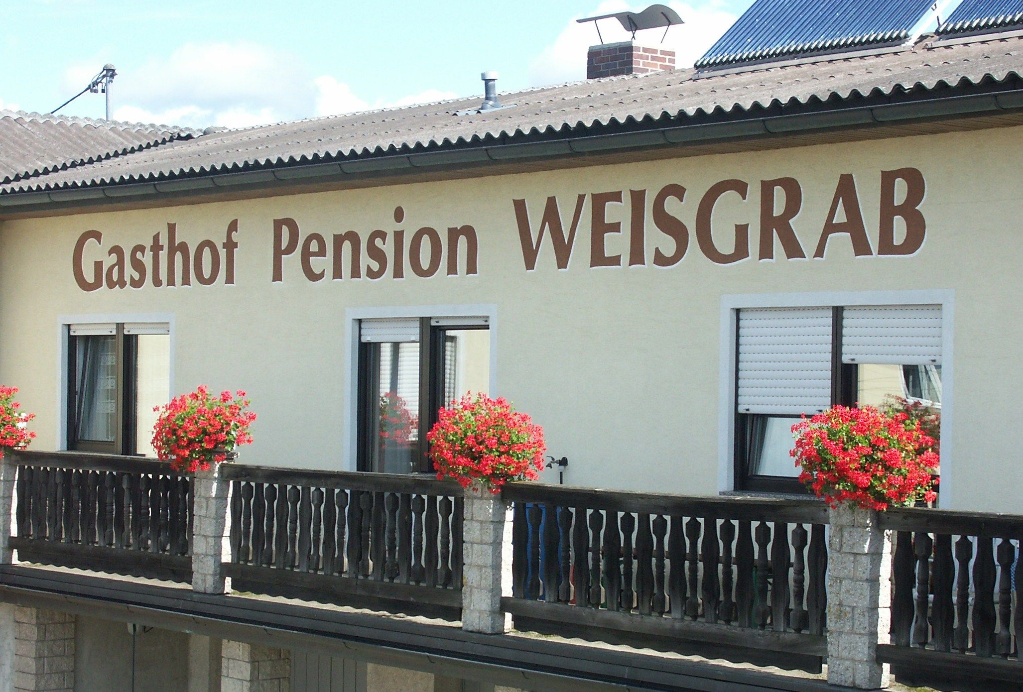 Fasáda penzionu Weisgrab s květinovými truhlíky na balkoně.