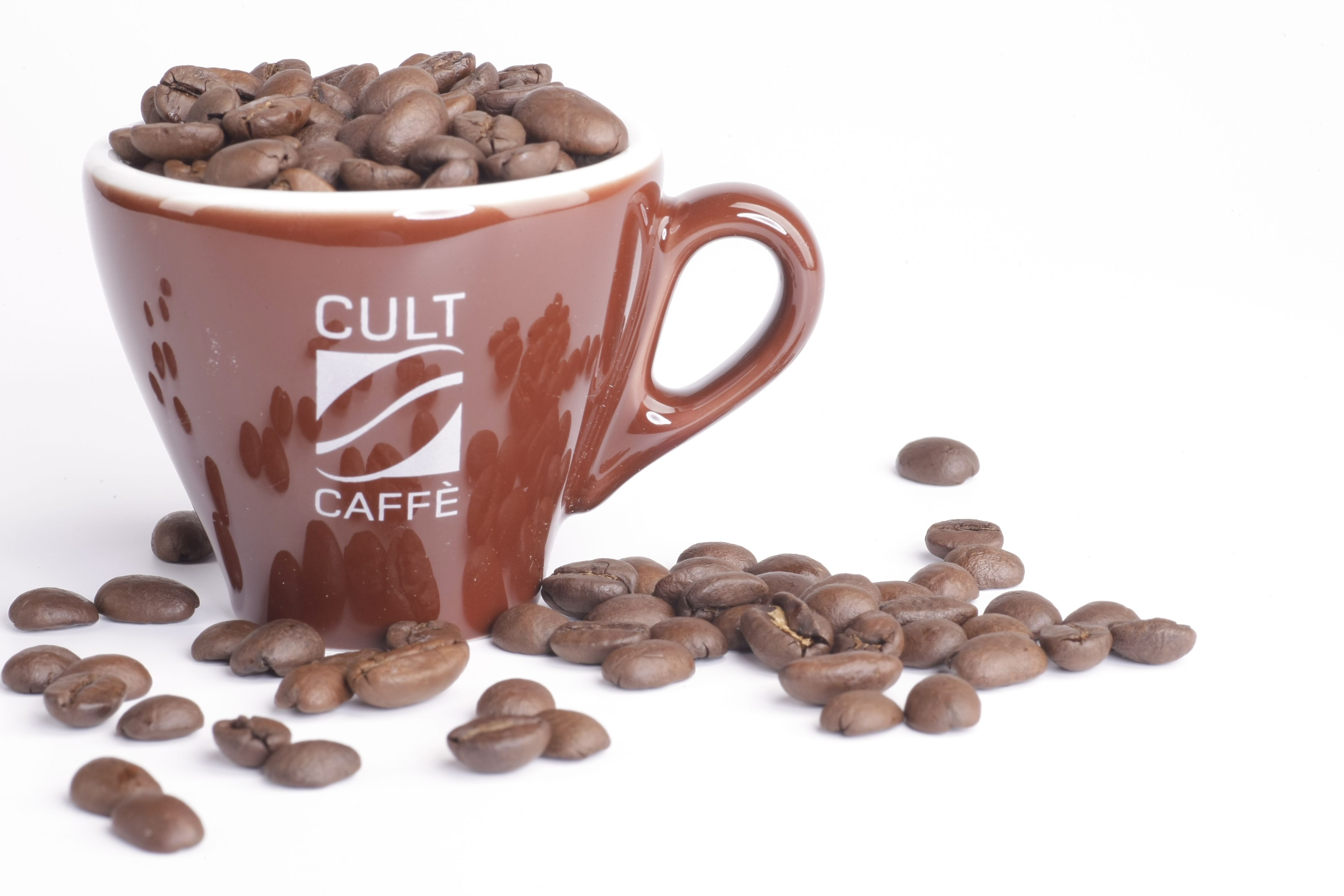 Hnědý hrnek s nápisem "Cult Caffè", naplněný zrnkovou kávou, na bílém pozadí.