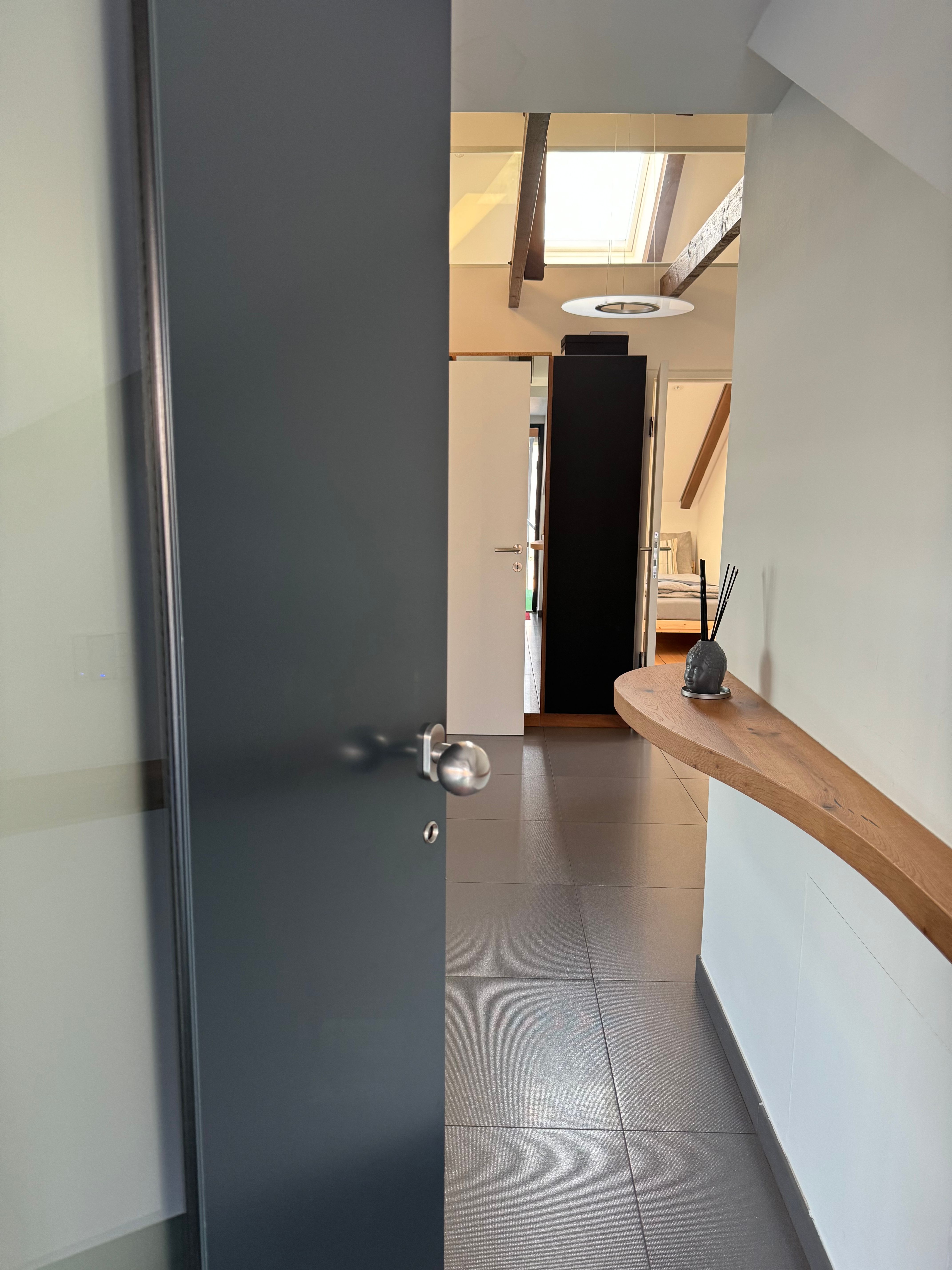 Moderní vstupní prostor s otevřenými dveřmi, dlážděnou podlahou a dřevěnou policí na stěně.