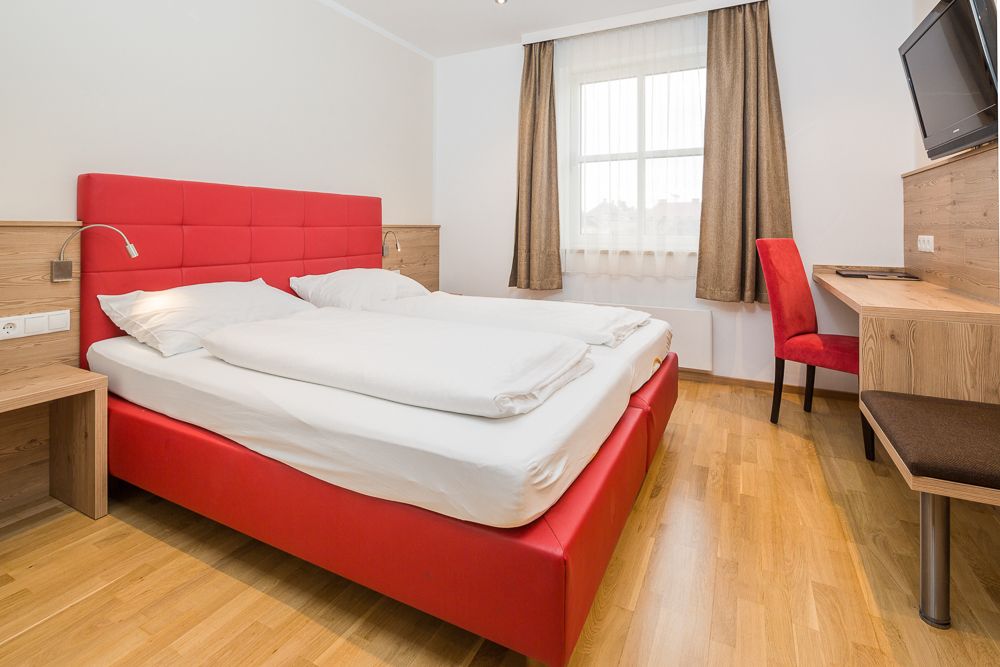 Moderní hotelový pokoj s červenou postelí a psacím stolem.