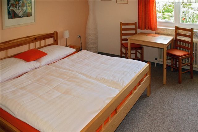 Útulný pokoj pro hosty s manželskou postelí, dřevěným nábytkem a malým stolkem u okna.