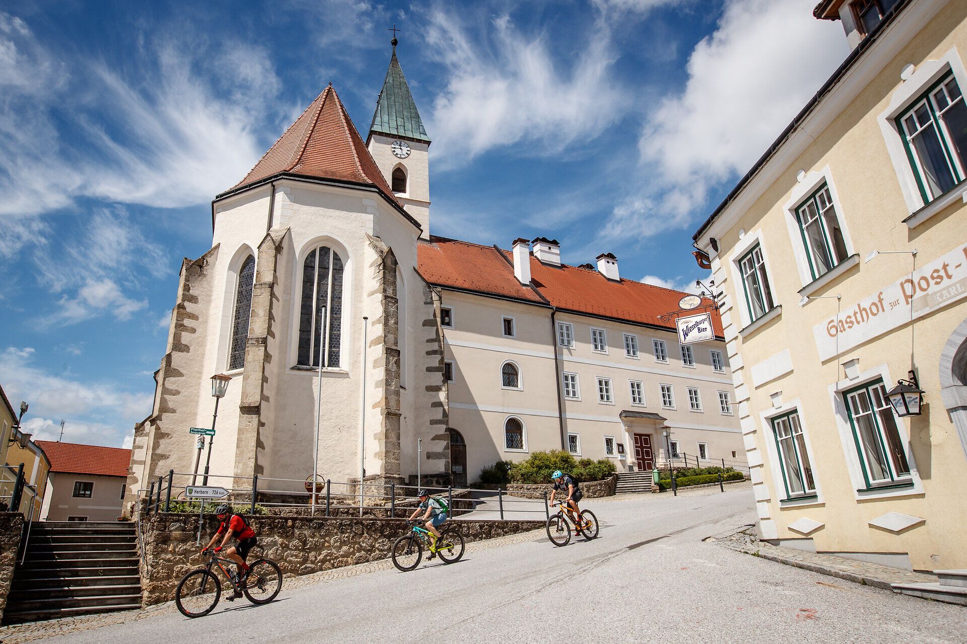 Zvlněné kopce vás zvou na nezapomenutelné dobrodružství a malebná architektura okolí tvoří harmonickou kulisu. Cyklisté kloužou po silnici, aby si vychutnali úchvatné výhledy na okolní přírodu. Zde, kde se setkávají tradice a příroda, je každý okamžik zážitkem.