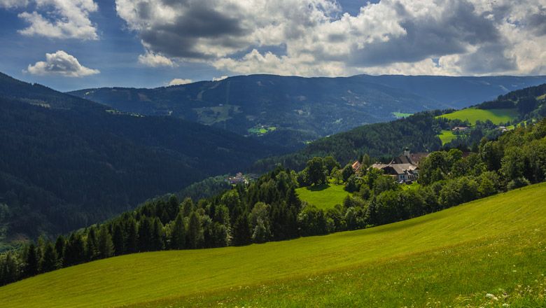 Zelené kopce a lesy v hornaté krajině pod zataženou oblohou.