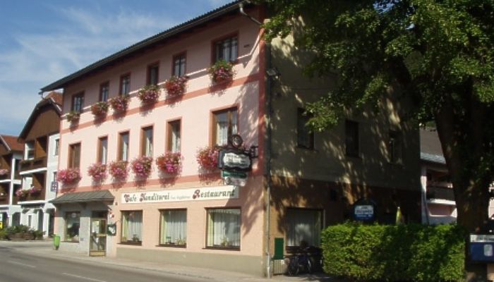 Tradiční hostinec s růžovou fasádou a květinovými truhlíky na oknech.