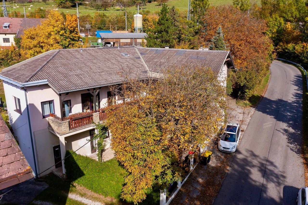 Letecký pohled na dvoupatrovou budovu s balkonem, obklopenou podzimními stromy a ulicí.