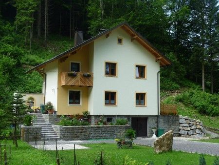 Žlutý penzion s dřevěným balkonem, obklopený zelenou přírodou a stromy.
