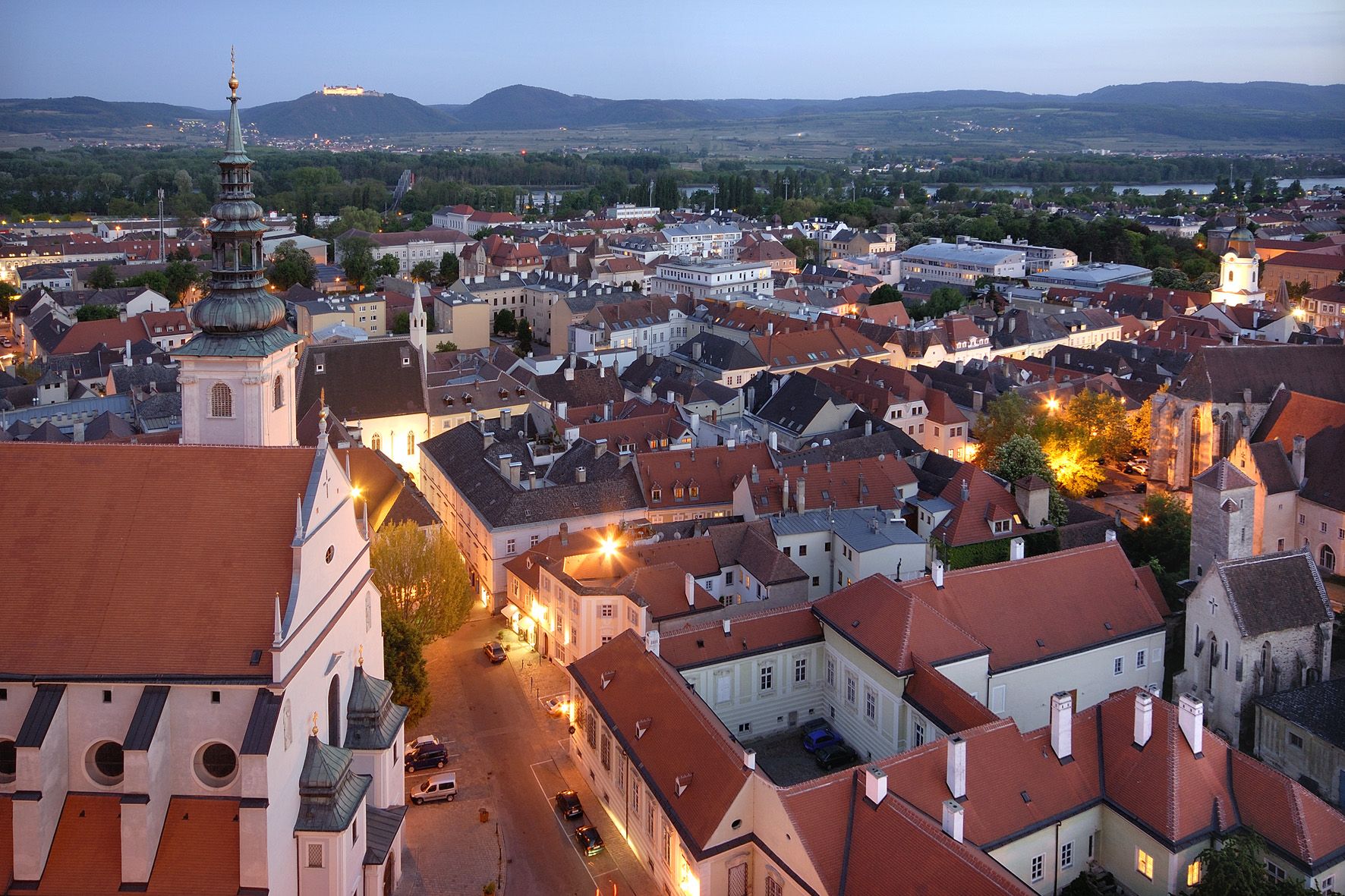 Večerní pohled na Krems s osvětlenými budovami a kopci v pozadí.