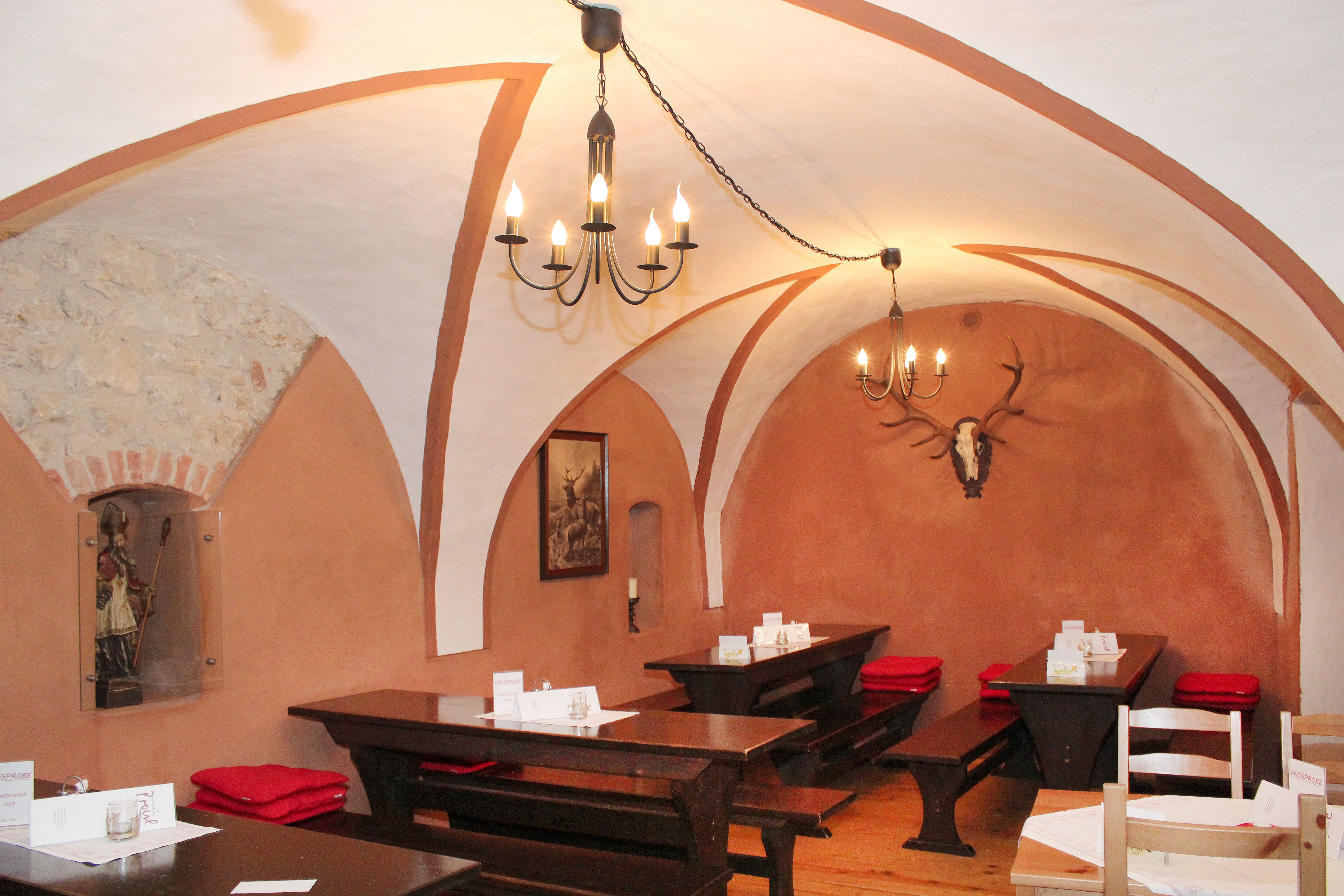 Rustikální restaurace s klenutým stropem, dřevěnými stoly a jeleními parohy na stěně.